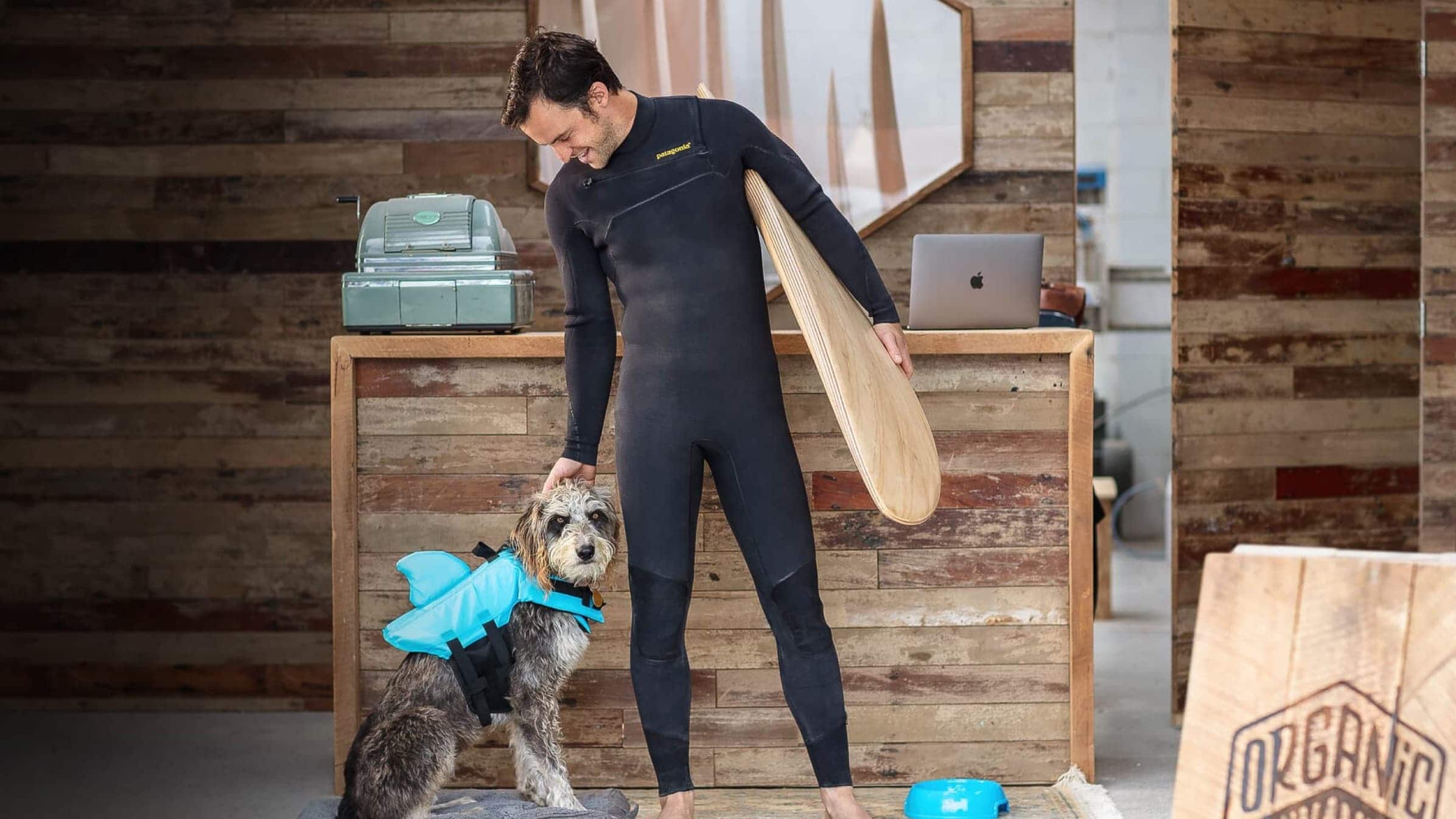 Jack Candlish, founder of Verdure Surf, wearing a … surfboard next to a dog wearing a swimming vest