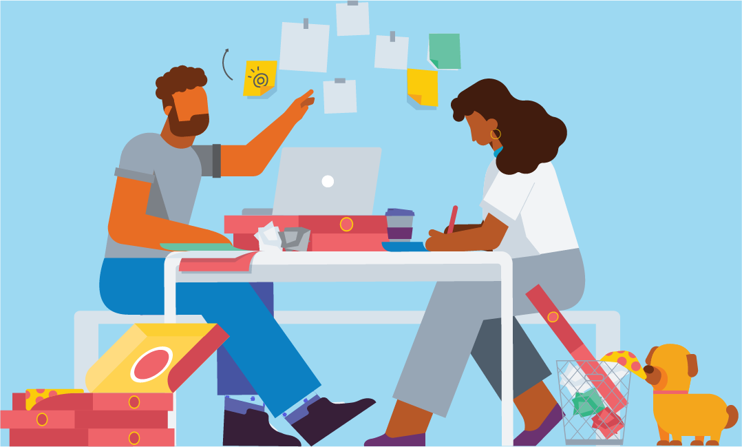 Two people sit working at a table next to a wall covered in post-it notes. The table contains a laptop and pizza boxes.